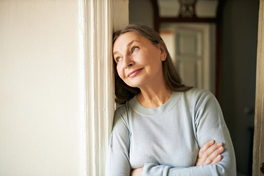 A woman in her forties lying in bed in early morning light, propped on one elbow and rubbing her eyes, sheets rumpled around her from a full night's sleep
