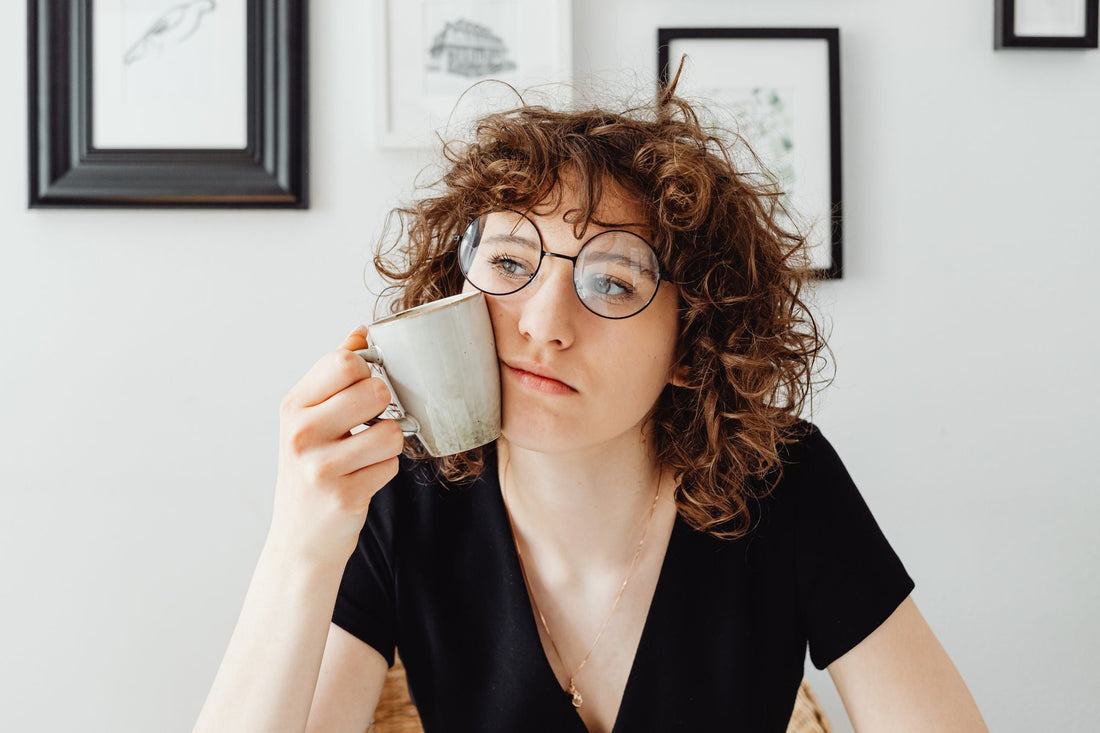 Tired woman holding a coffee mug against her cheek, looking weary
