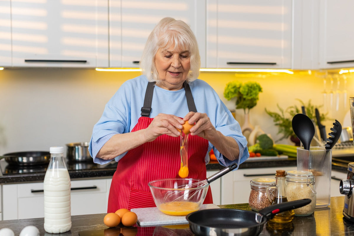A woman with white hair cracking an egg into a glass bowl in her home kitchen