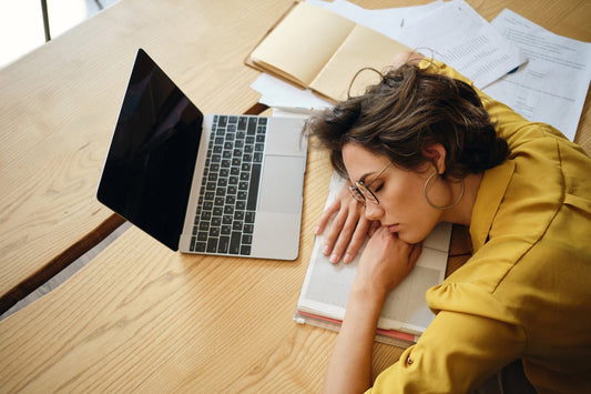 Tired woman asleep at her desk beside a laptop and paperwork, worn out in the afternoon